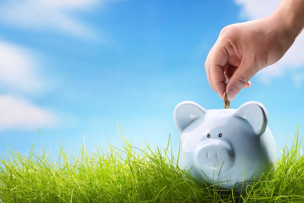white piggy bank on green grass with light blue sky and clouds in the background; savings concept