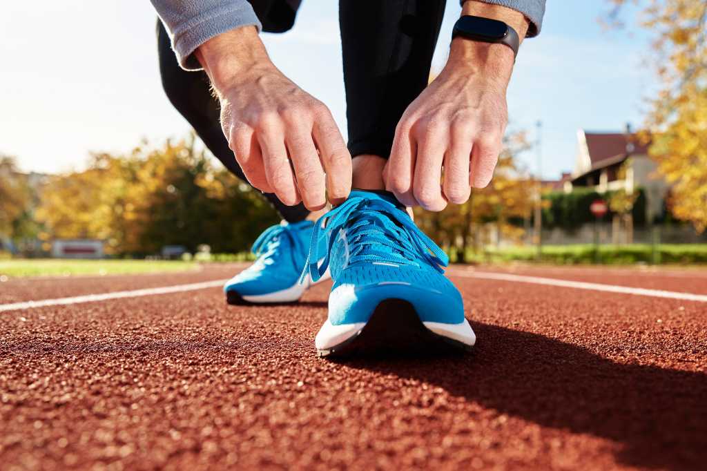 Person kneels to tie their blue track shoes before a run.