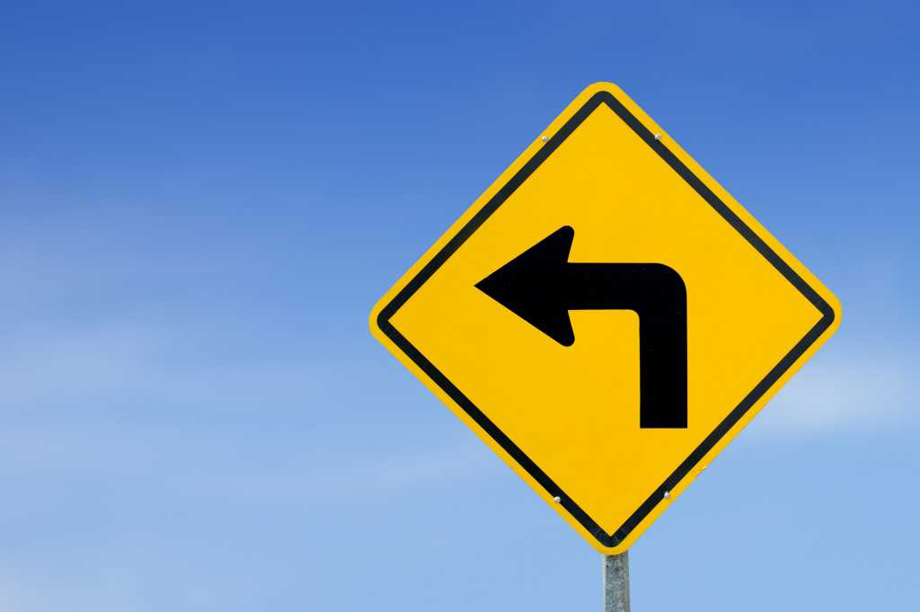 Left turn coming. Yellow traffic sign turn left against a blue sky background.