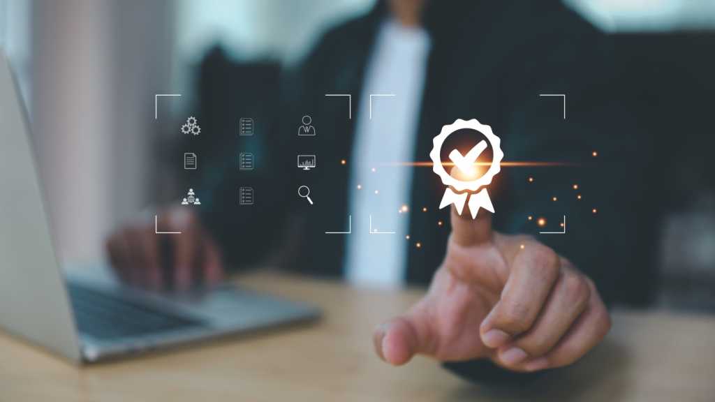 A photograph of a man sitting in front of a laptop. He is pointing his figure at a floating icon of a symbol representing a certificate, with gold sparkles coming out of his finger. To the left of the certificate icon are nine smaller icons.